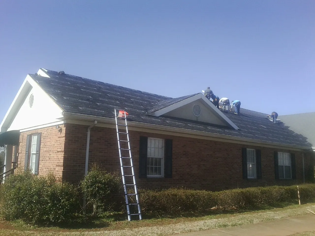 Crew tearing shingles off a brick ranch roof with a ladder set — Emergency Roof Repair work by our crew in Twain