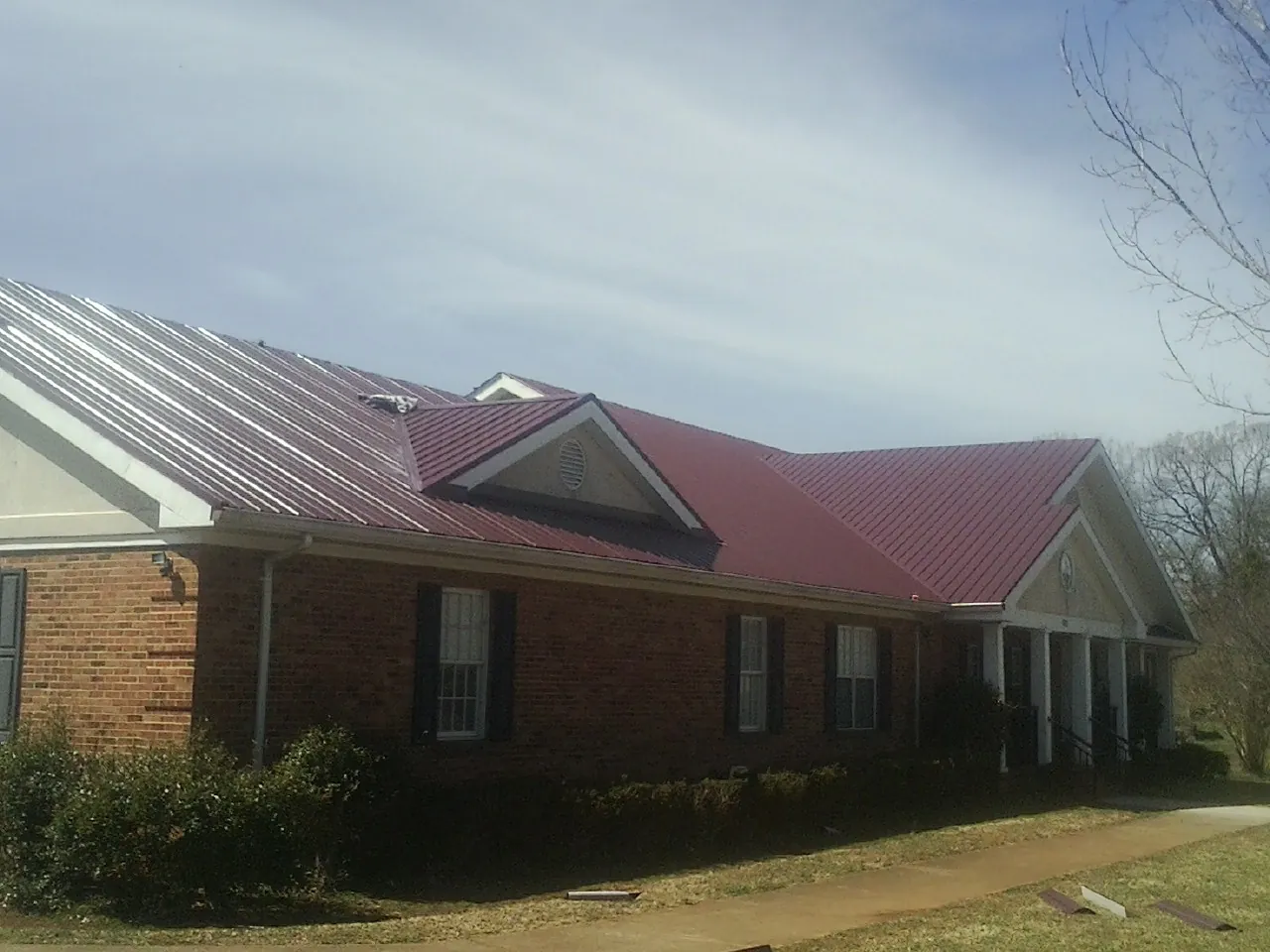 Red metal roof with gabled entries on a long brick building, from a Hail Damage Roof Repair job in Twain
