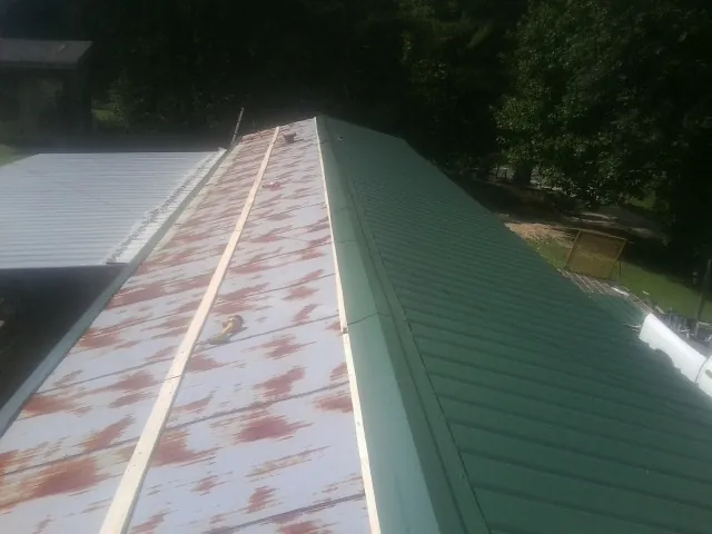 Old rusted panels beside newly installed green metal roofing — Wind Damage Roof Repair by Roofing Brothers in Twain
