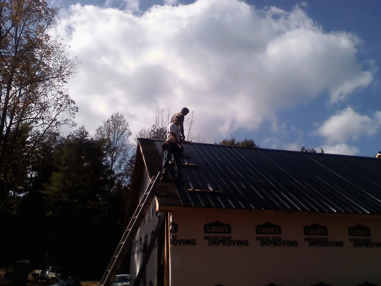 Roofer fastening dark metal panels high against a cloudy sky, from a Roof Inspection job in Twain